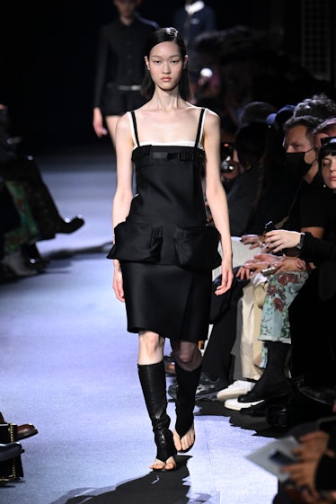 A model wearing Miu Miu black dress with oversized pockets and sandal high boots at Paris Fashion We...