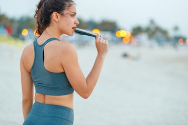 Female jogger in sports bra standing on a break and biting protein bar