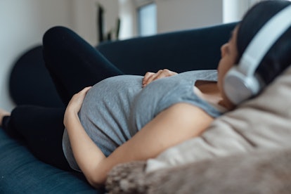  pregnant woman listening tomusic with headphone while resting at home in an article about can sex t...
