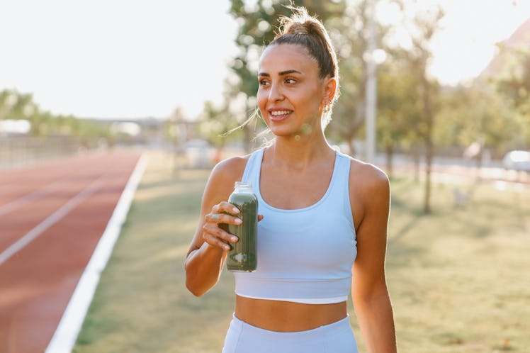 Sporty woman drinking detox green smoothie in the Park. Green smoothie woman drinking plastic cup br...