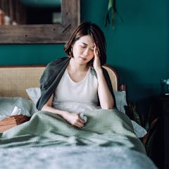 Young Asian woman staying at home and lying in bed, feeling sick with her hand on her head, with med...