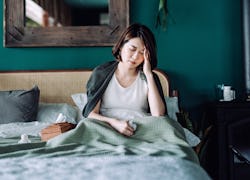 Young Asian woman staying at home and lying in bed, feeling sick with her hand on her head, with med...