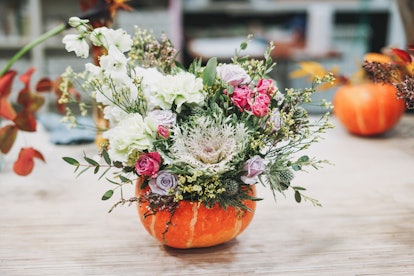 A pumpkin flower arrangement showcasing an array of white, lavender, and pink flowers with greenery ...