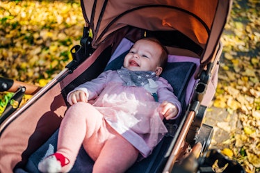 Baby girl in a stroller in an autumn park surrounded by fallen leaves.
