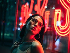 young woman standing near neon lights on the street, poses for a photo as she reflects on the novemb...