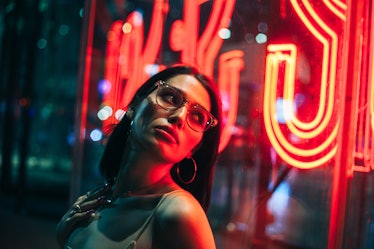 young woman standing near neon lights on the street, poses for a photo as she reflects on the novemb...