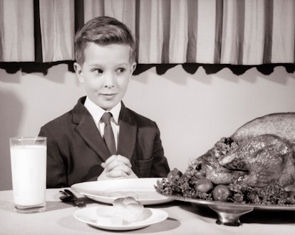 1950s 1960s boy wearing suit and tie sitting at table hands clasped saying grace looking hungrily at...