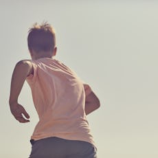A young boy runs against a warm blue sky. A back point of view with oy running away from camera into...