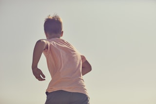 A young boy runs against a warm blue sky. A back point of view with oy running away from camera into...