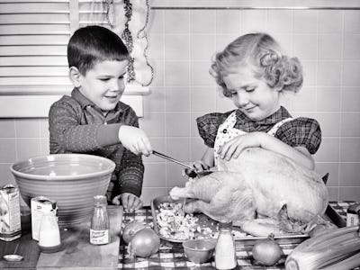1950s SMILING BOY AND GIRL BROTHER AND OLDER SISTER LADLING BREAD STUFFING INTO THANKSGIVING TURKEY ...