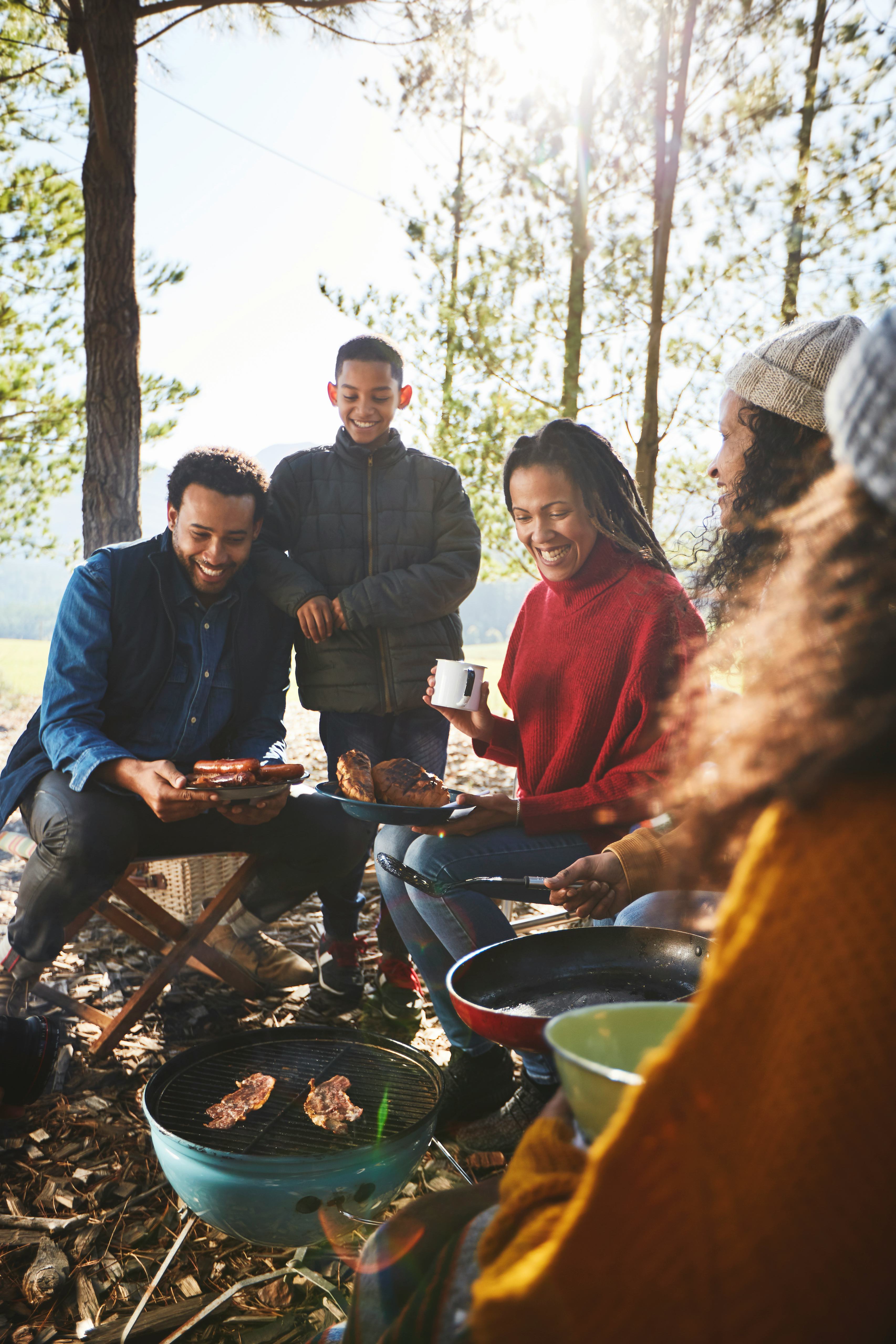 A family roasting hot dogs around campsite barbecue grill on a fall camping trip.