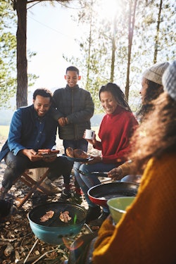A family roasting hot dogs around campsite barbecue grill on a fall camping trip.
