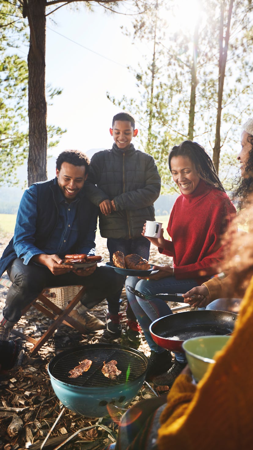 A family roasting hot dogs around campsite barbecue grill on a fall camping trip.