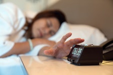 A woman pressing the stop button on her alarm clock.