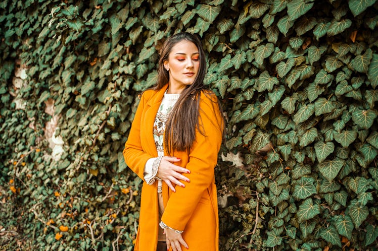 young woman posing in an orange coat as she thinks about her november 21, 2022 weekly horoscope 