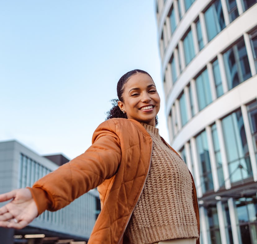 young woman smiles and opens her arms wide as she considers her november 23, 2022 weekly horoscope