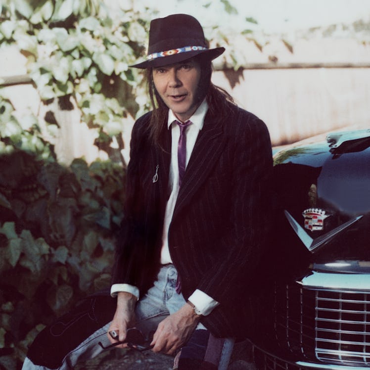Neil Young sitting on bumper on 1950s Cadillac in Los Angeles, California, 1988 (Photo by Aaron Rapo...