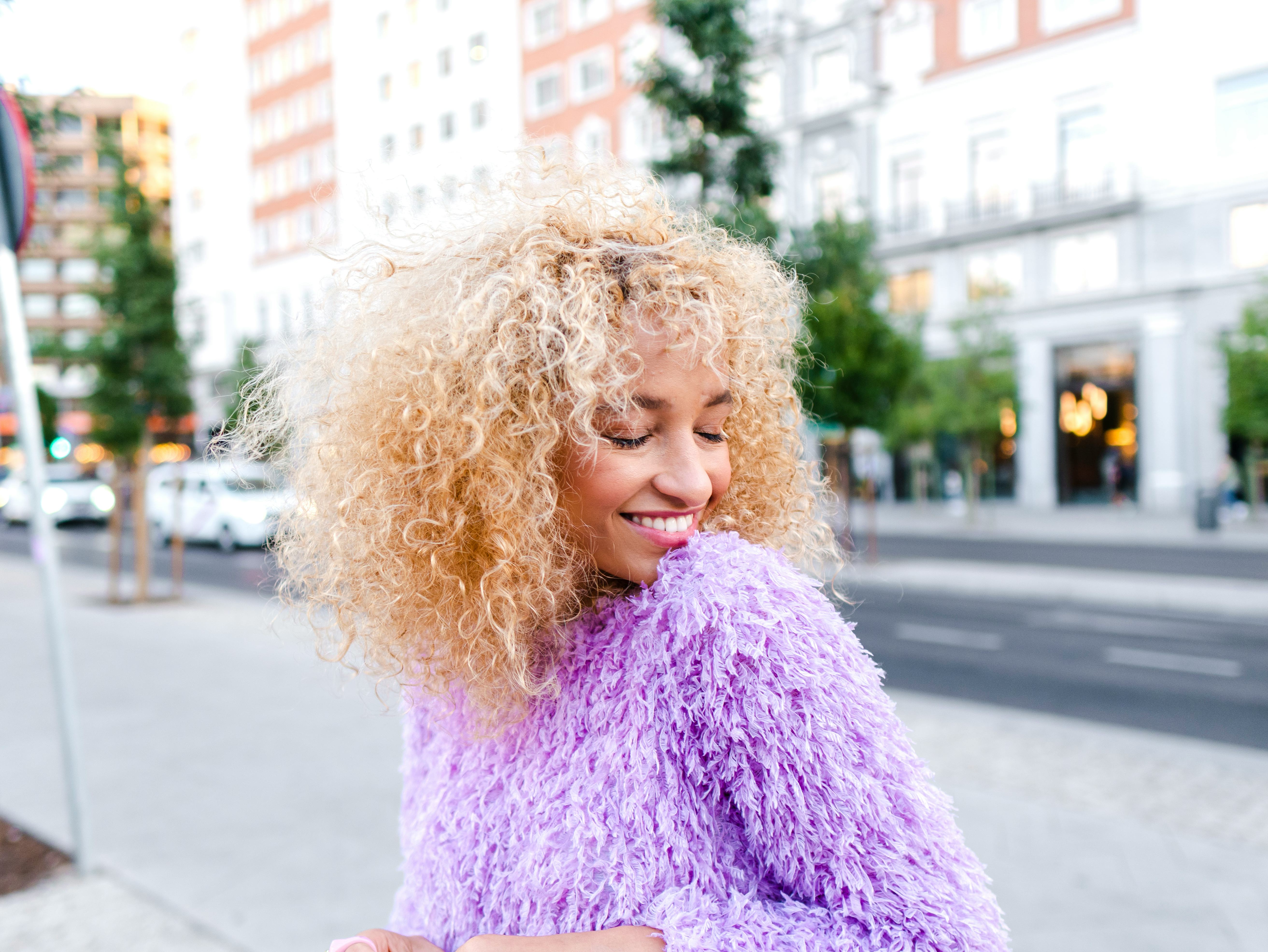 young woman wearing bright purple sweater smiles in the street as she considers how jupiter retrogra...