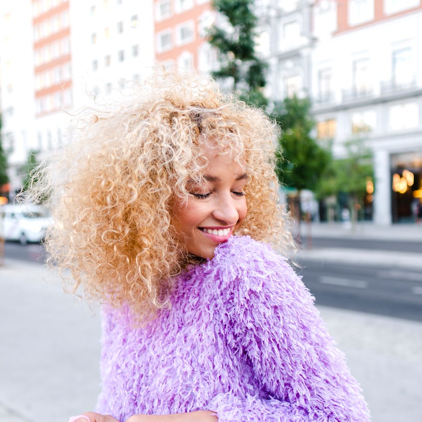 young woman wearing bright purple sweater smiles in the street as she considers how jupiter retrogra...