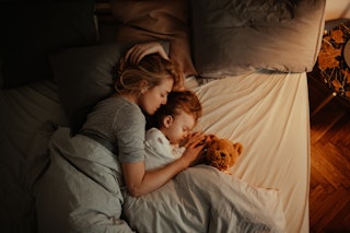 Beautiful mother and daughter sleeping together in bed. It is the evening and there is lamp on. Mom ...