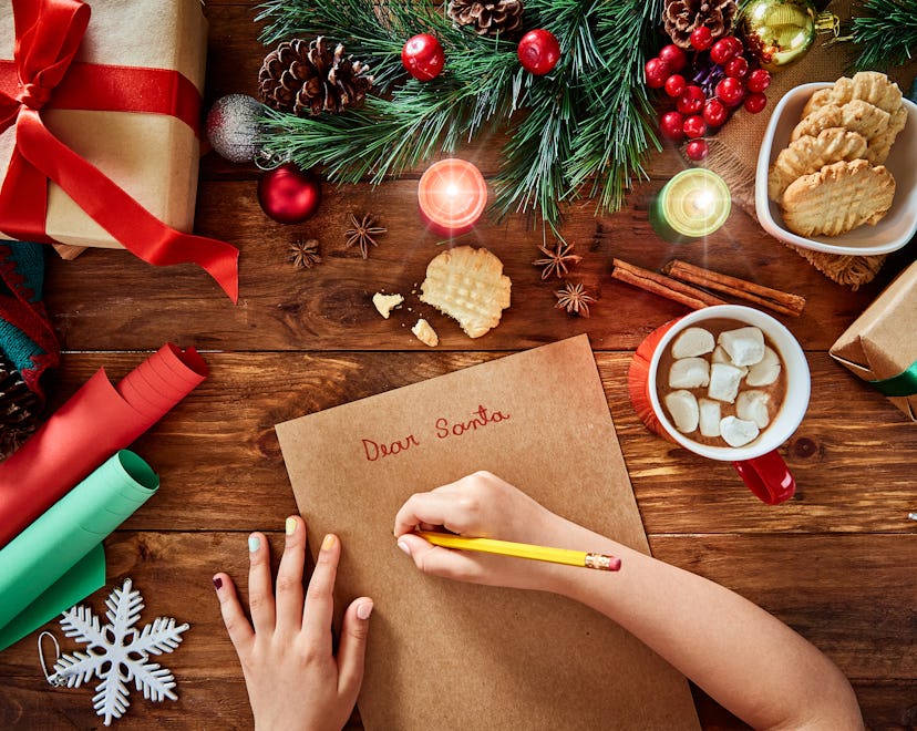 Christmas concept: Top view of kid hands writing wish list and Christmas gifts on rustic wooden tabl...