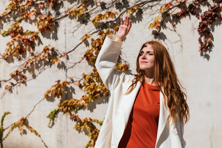 a young woman reaches her hand above her head and blocks the suns rays as she considers her november...