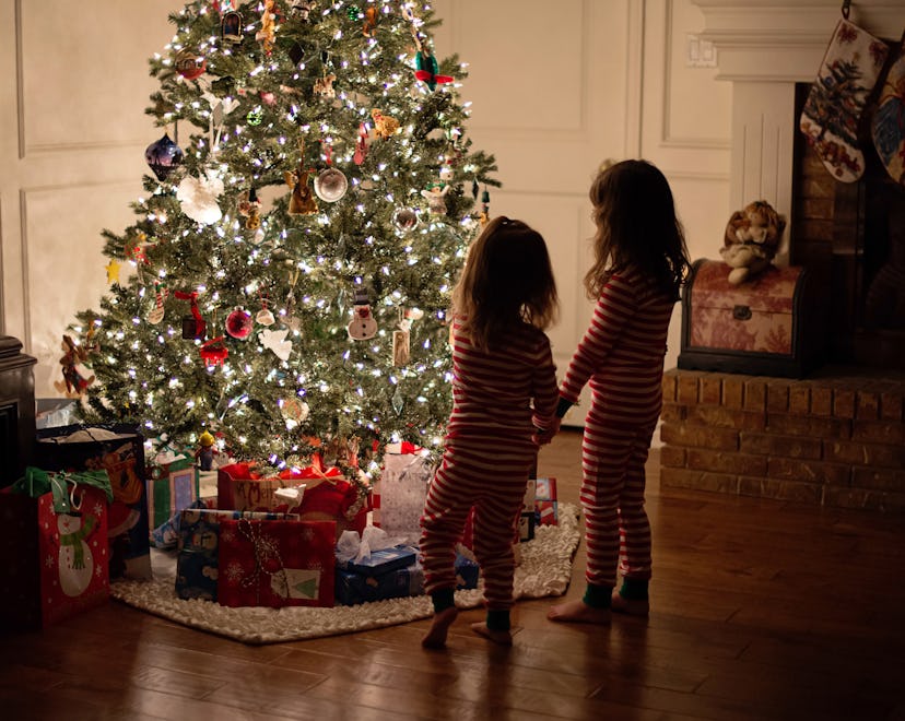 a lit tree with little kids looking at it in an article about is it safe to leave a christmas tree ...