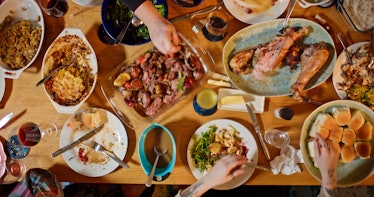 Overhead shot of people gathered around a dining table loaded with food at a Friendsgiving potluck d...