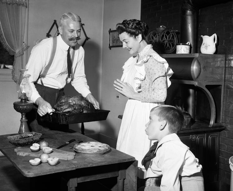 1890s 1900s MOCK TURN OF THE 20TH CENTURY THANKSGIVING DINNER FATHER TAKING TURKEY OUT OF STOVE SHOW...