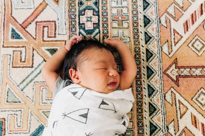 a baby with arms out of the swaddle in an article about when to stop swaddling and transition to a s...
