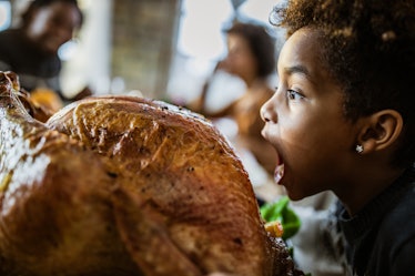 A little girl about to bite directly into a Turkey prepared for a Thanksgiving meal