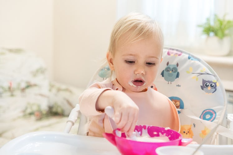 Toddler in high chair eats porridge from a spoon.