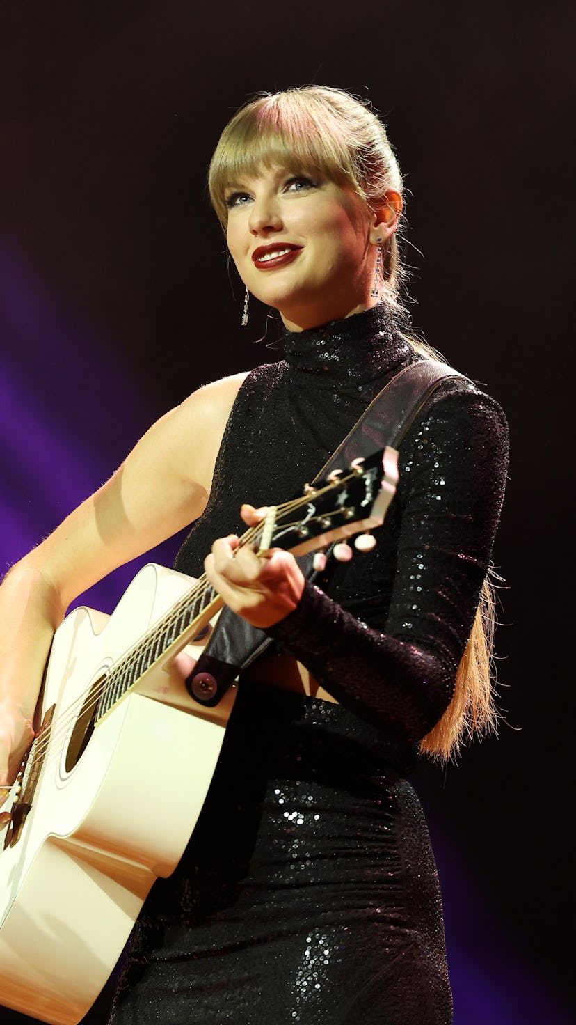 Taylor Swift smiling and holding a guitar live onstage