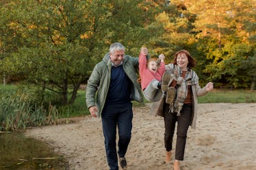 A grandpa and grandma swinging their grandchild with their arms while walking outside on a fall day.