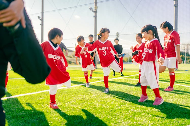 Members of female kids' soccer or football team are warming up before starting training.