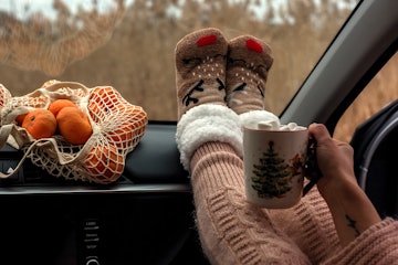 Close-up of women's legs in warm wool socks on the dashboard of the car. Next to a mug with coffee o...