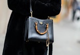 PARIS, FRANCE - JANUARY 25: A guest wears a black fur long coat, a black shiny leather Diana crossbo...