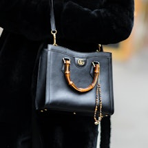 PARIS, FRANCE - JANUARY 25: A guest wears a black fur long coat, a black shiny leather Diana crossbo...