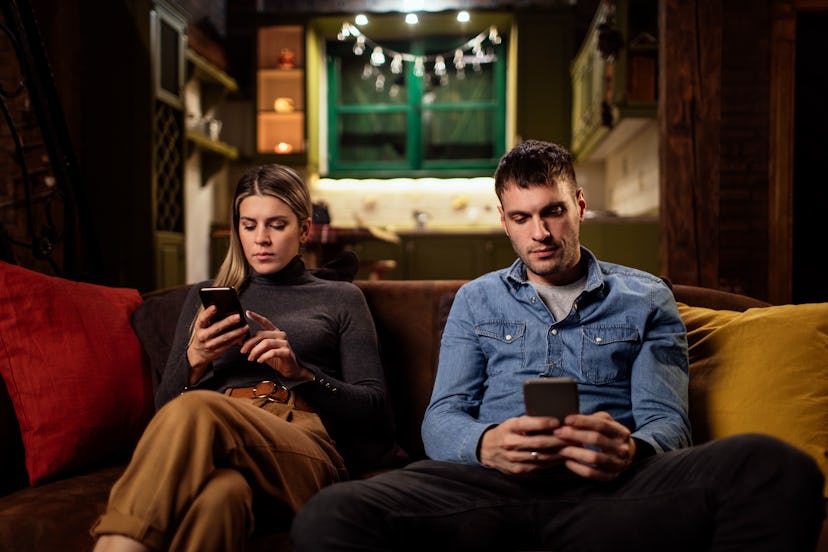 Young man and woman using their phones while sitting on their couch 