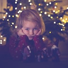 Cute little danish girl with blond hair laying alone and bored in front of Christmas tree due to cov...