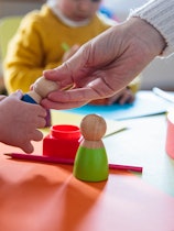 An adult handing a child a toy at a day care center. A new study suggests that spending more time at...