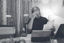 A bald young man is looking worried while going through his bills at home.