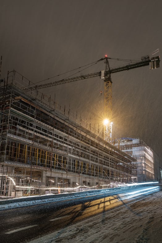 Evening view of construction site with large crane. Snow in the air and on the ground