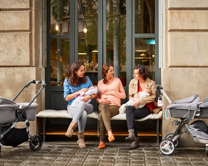 Expectant sitting amidst friends carrying babies outside restaurant