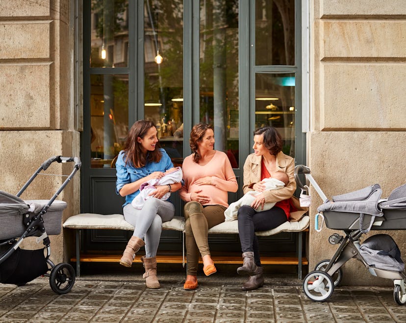Expectant sitting amidst friends carrying babies outside restaurant