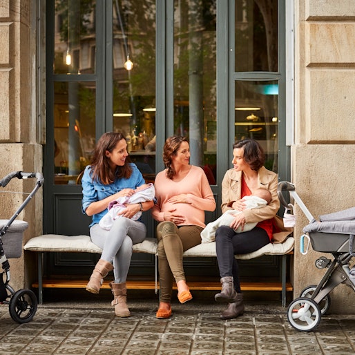 Expectant sitting amidst friends carrying babies outside restaurant