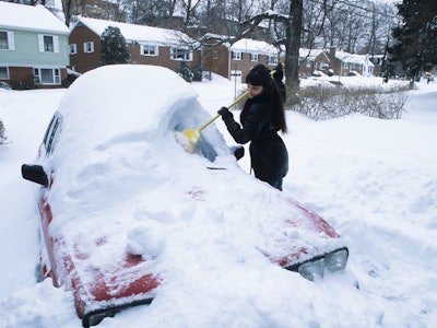Woman brushing snow off car after snow storm - Arlington, Virginia, USA.