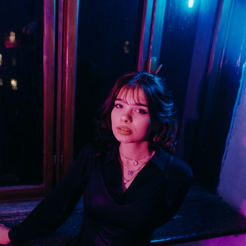 young woman poses in front of an open window as she considers her december 12, 2022 weekly horoscope
