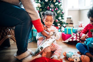 A woman helps her daughter open presents in the living room on Christmas morning in front of the tre...