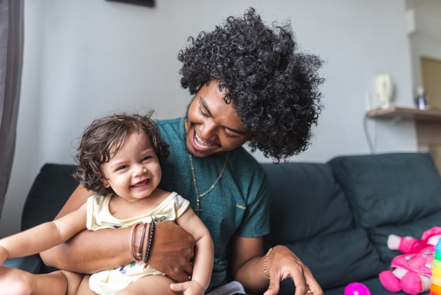 Young father playing with his baby daughter on the couch in apartment living room in article about N...
